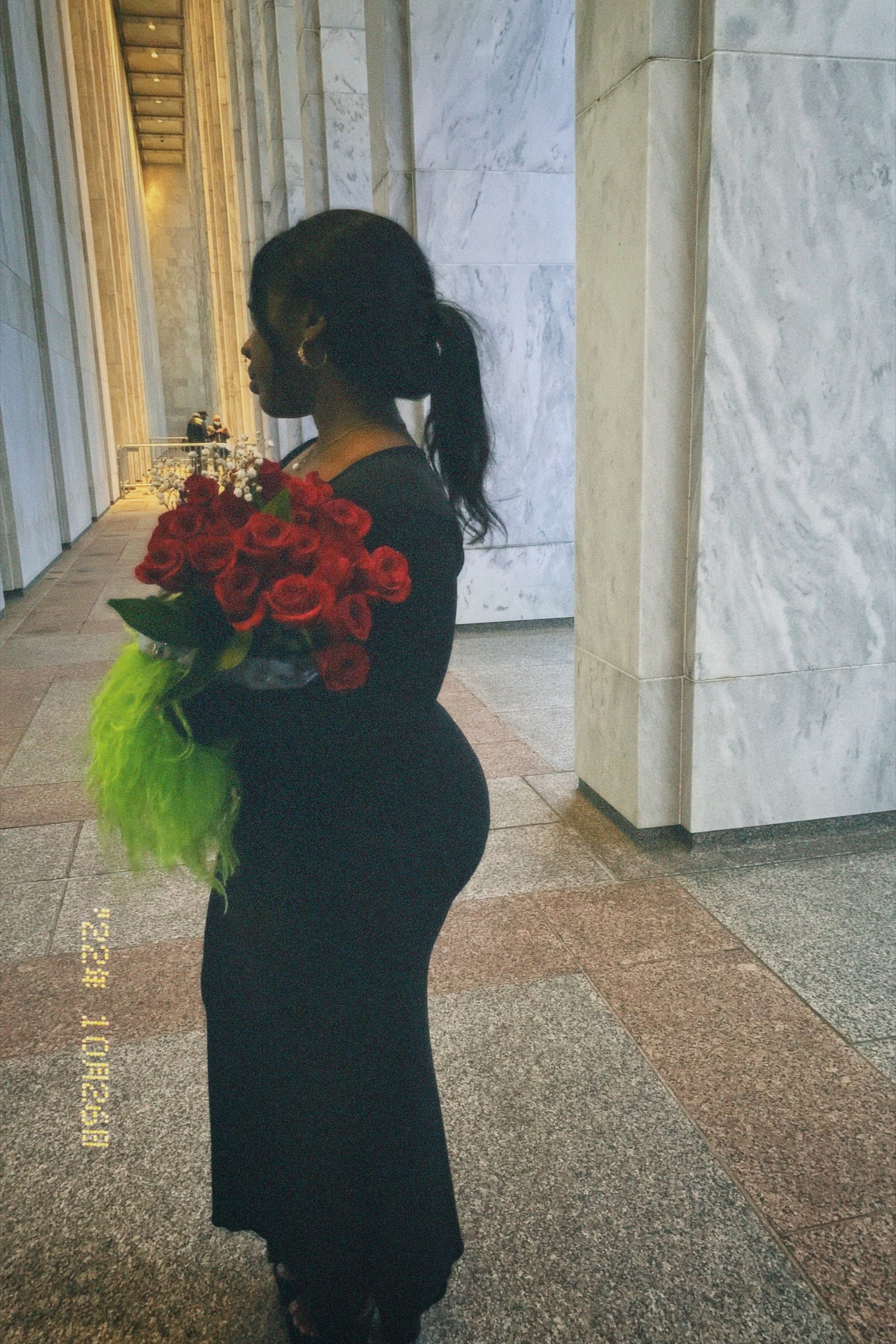 Black woman in black maxi dress with green feathered sleeves holding red roses